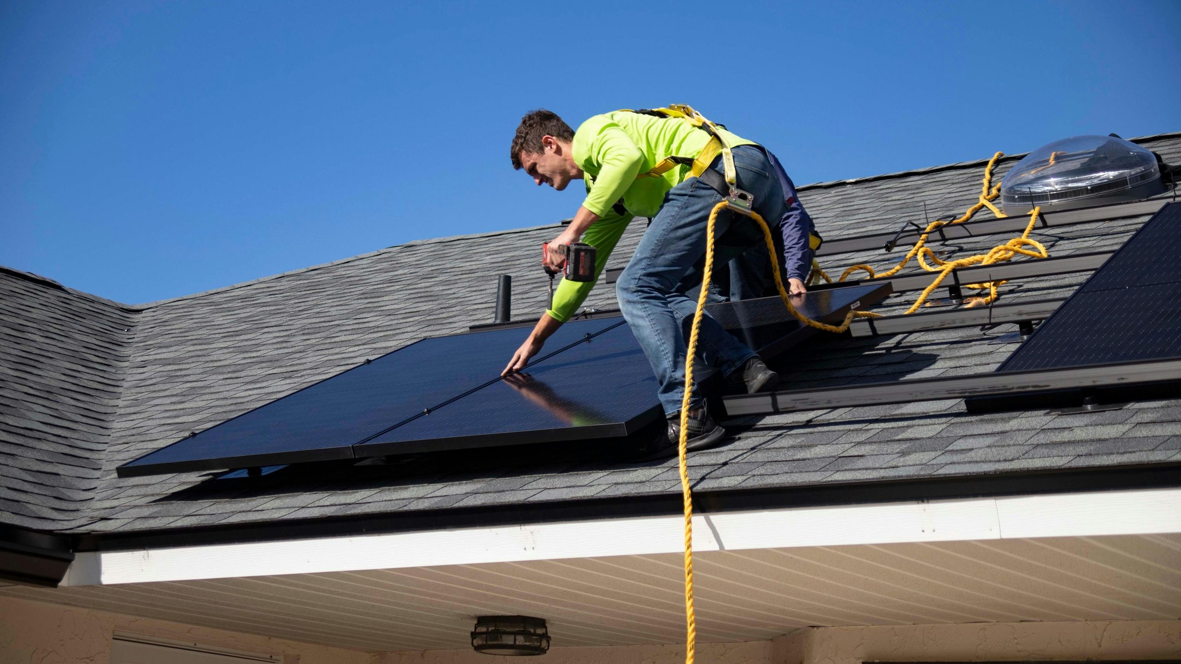 An installer in hi-vis fixing a black solar panel onto a pitched roof