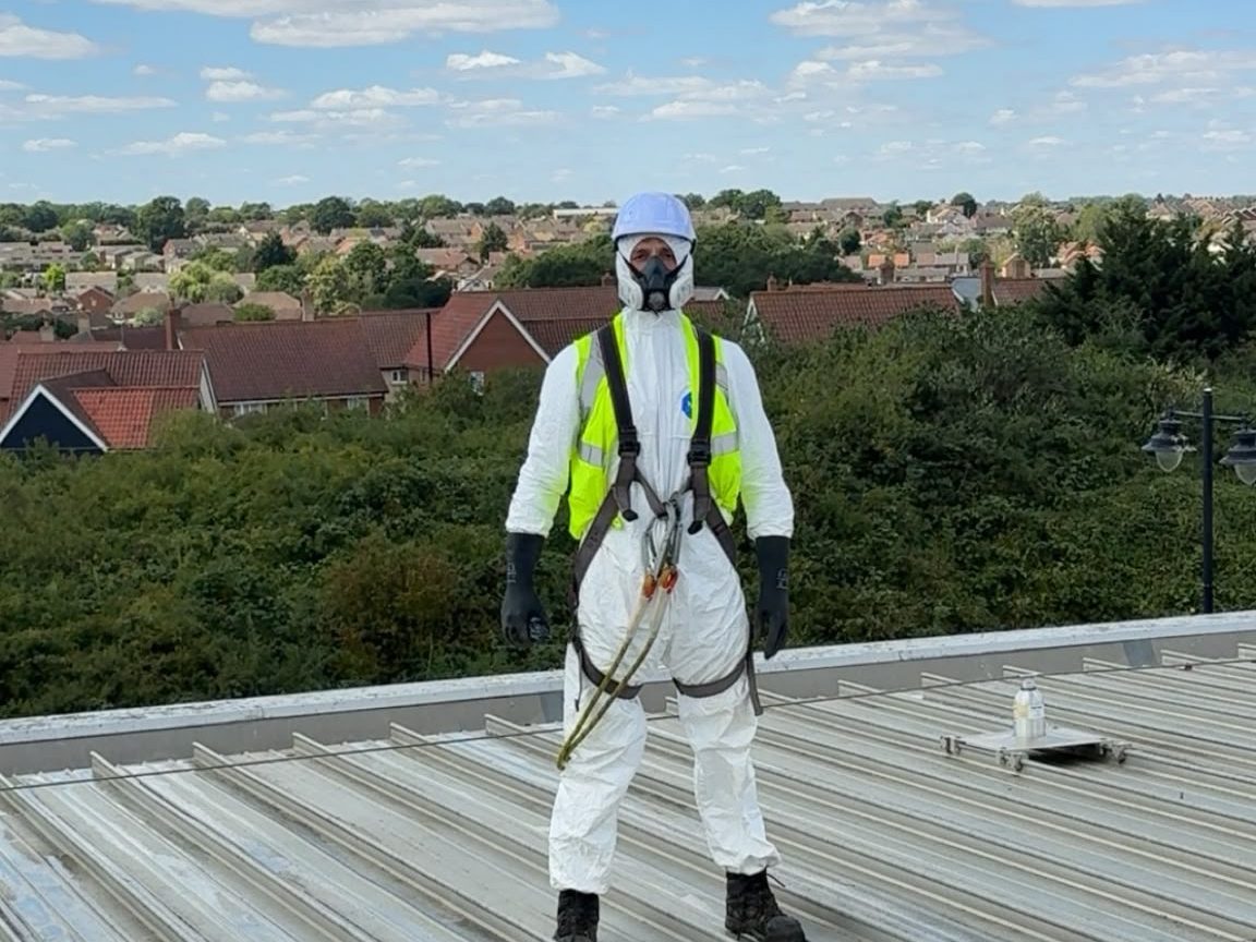 A technician in safety harness and protective suit on a commercial solar roof