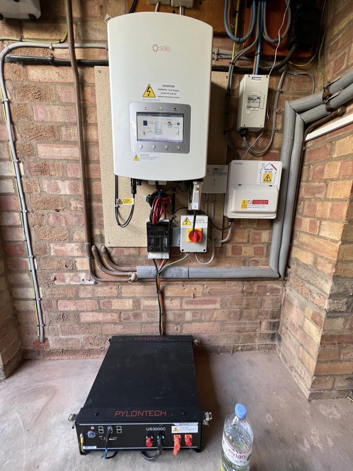 A battery inverter on the wall with its battery waiting below, part way through an installation